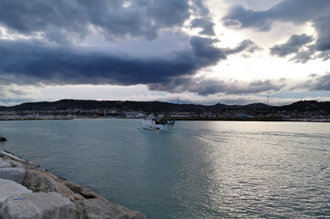 Passaggio barca cielo mare nuvole scure sera porto scogli riflessi acqua