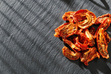 Red sun dried tomatoes with sunlight and shadow on black background. Tasty small slices tomato with spices and olive oil.