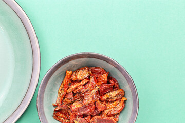 Red sun dried tomatoes in ceramic plate on colored background. Tasty small slices tomato with spices and olive oil.