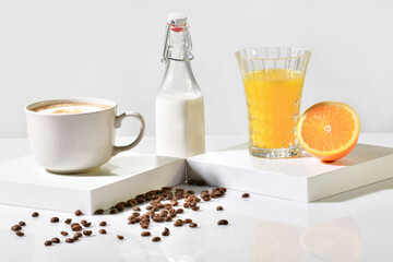 Roasted coffee beans surrounded by fresh orange juice, a bottle of milk and a cup of coffee on a light background. Coffee and fruit concept.