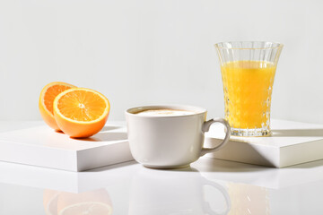 A cup of freshly made coffee between an orange cut in half and a glass of orange juice