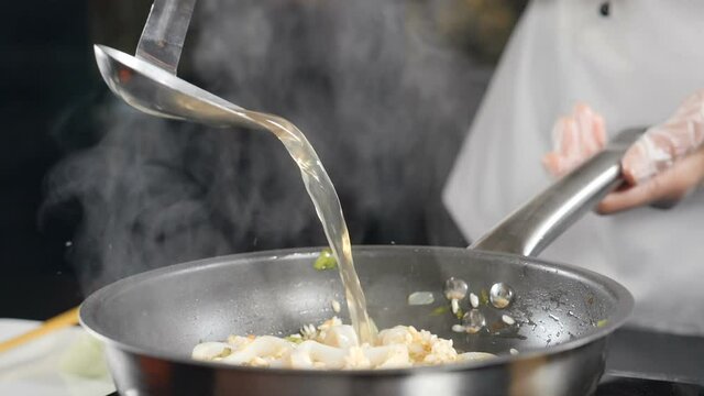 Italian seafood restaurant. Close-up shot of chef pouring fish broth from ladle into risotto. Slow motion. Traditional Italian cuisine. Full hd