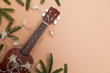 Festive composition ukulele guitar fir branches and lights of Christmas garland on a beige...