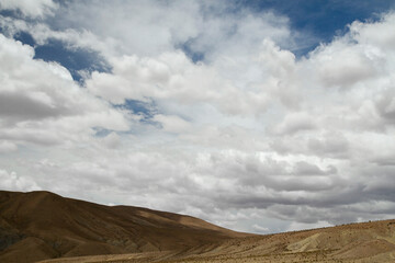 Desert landscape. View of the arid hills and brown valley under a beautiful summer sky with white clouds.