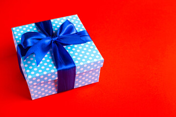 Blue gift box with a bow on a red background. Holiday greeting card.