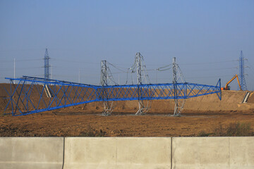 The power line support lies on its side against the background of an operating power line and a blue sky.