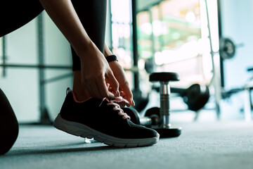Fototapeta na wymiar woman's hands tying shoelaces on sport sneakers in gym. dumbbell and water bottle on the ground around the sport girl.