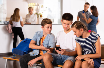 Group of three teenage schoolmates with smartphones on break in college