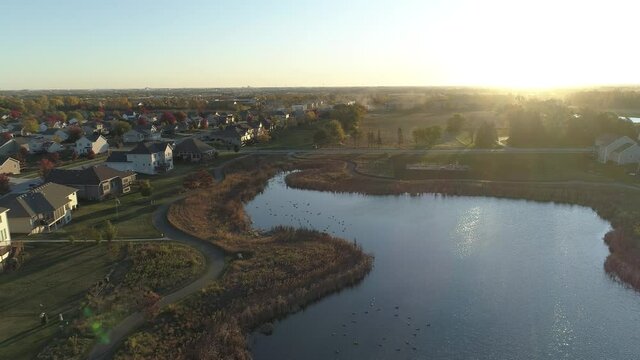 Reverse-dolly aerial shot of pond and residential neighborhood at sunrise.