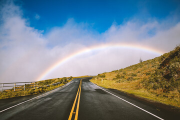 Rainbow over the road, Haleakala Highway, Maui, Hawaii. The Haleakalā Highway is a scenic, winding road on Maui that climbs to the summit of the Haleakalā volcano in Haleakalā National Park