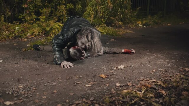 Male zombie killing man lying on road during apocalypse