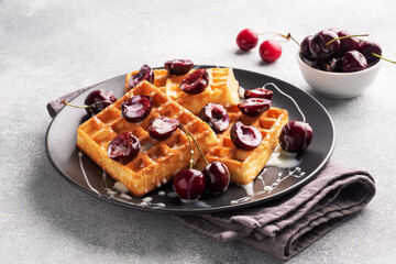 Belgian fluted waffles with fresh cherries and cream on a plate. Soft homemade waffles, sweet dessert with cherries. copy space