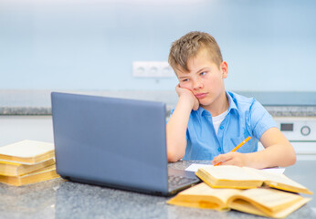 The boy is studying online with the help of a notubuck, clinging to books in the kitchen and...