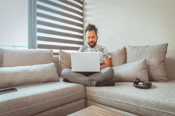 joven mexicano trabajando desde casa en sofa con computadora personal comodo