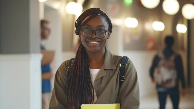 Happy university african student holding books standing in corridor