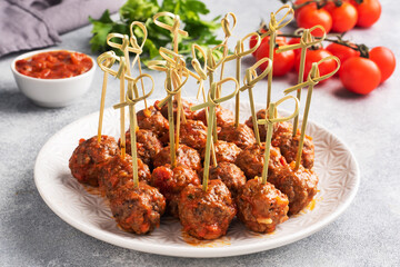 Beef meatballs stewed in tomato sauce on a plate on barbecue skewers. Light concrete background.