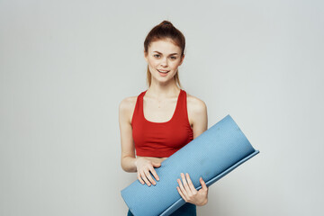 Woman holds in hand a mat for fitness sport slim figure exercises light background