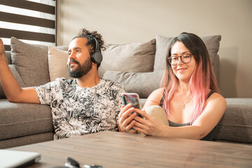 joven pareja mexicana pasan tiempo juntos en casa sala sofa escuchando musica y usando el telefono