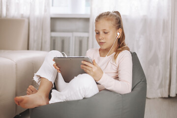 Puzzled teenage girl sitting in beanbag chair in white room doing homework with tablet, online education, distance learning, technology concept