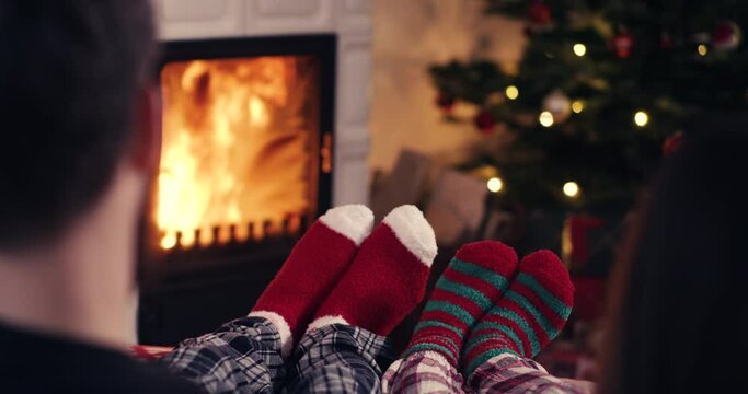 Couple feet in cozy christmas woolen socks near fireplace with decorated christmas tree in background shot in 4k