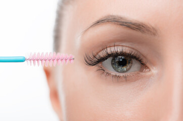 A beautiful light-skinned girl with beautiful eyes combs her extended eyelashes with an eyelash...