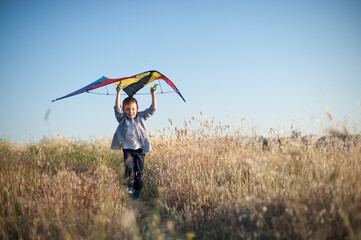 active little boy running with kite above head among dry grass field with copy space