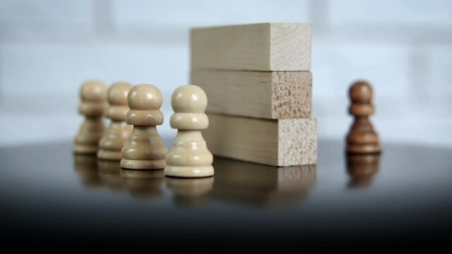 Segregation concept. White chess pawns stand behind the wall from the black pawn.