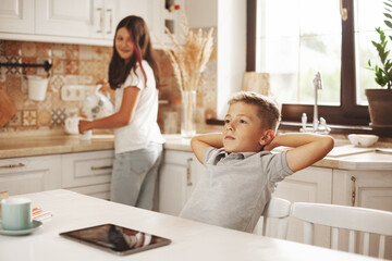 Fototapeta premium A tired boy pulls himself up after online lessons in the kitchen at home, his sister helps him. Distance learning, online education, home schooling concept