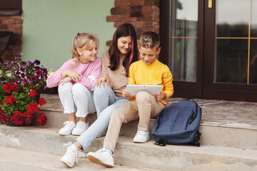 A group of happy teenage children after school sit on the steps and play on a digital tablet. Modern children, digital technologies