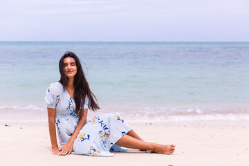 Fototapeta na wymiar Romantic portrait of woman in long blue dress on beach by sea at windy day. 