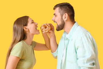 Young couple with sweet donut on color background