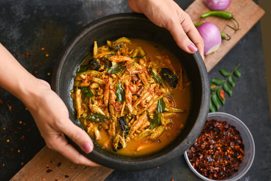 Top view spicy hot anchovy Kerala fish curry. Indian food. Woman hand making Fish curry with red chili, curry leaf, coconut milk. Asian cuisine. Delicious spicy , Bengali , Goan fish curry in clay pot