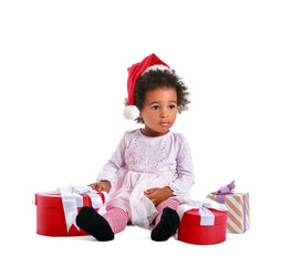 Cute African-American baby girl in Santa hat and with Christmas gifts on white background