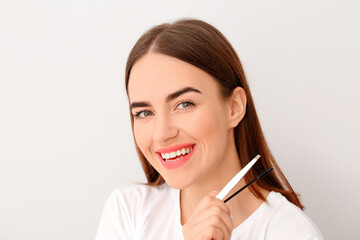 Young woman with tools for eyebrow correction procedure on light background