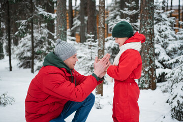 Fototapeta na wymiar After playing in the open air in the winter in the woods, the boy's hands froze and his father sat down in front of him to warm him up.