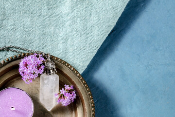 Clear quartz crystal charm with vervain flowers and a scented candle, shot from the top with copy space on a blue background