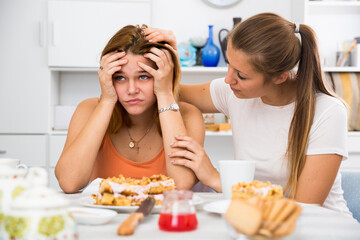 Obraz na płótnie Canvas Portrait of female talking with sad girl friend at the kitchen