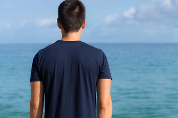 Pensive young man standing looking towards the ocean horizon view. 