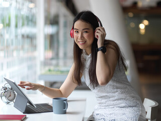 Portrait of female relaxing with headphone and tablet in co working space