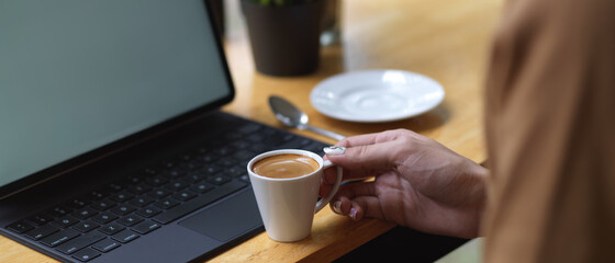 Female hand holding coffee cup on wooden bar with digital tablet in cafe