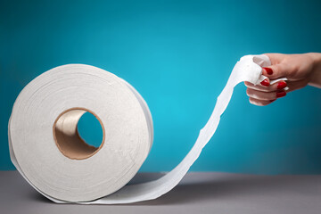 Hand holding the edge of a roll of toilet paper, on a blue background close-up. The concept of...