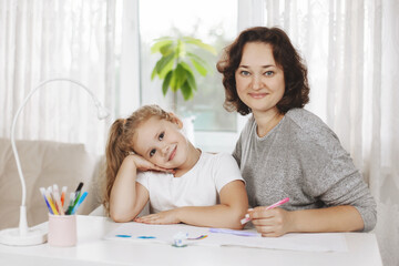 Obraz na płótnie Canvas Mom helps her little daughter do her homework. Mom teaches the girl to draw. Home training, online training