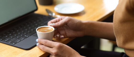 Fototapeta na wymiar Side view of female hands holding coffee cup while sitting at workplace