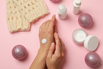 Female hands with cosmetic cream on pink background with Christmas accessories
