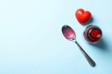 Bottle and spoon with syrup and heart on blue background