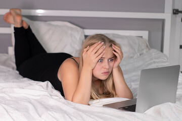 attractive cute shocked surprised blonde with laptop on bed with white sheets. pretty people at isolation.