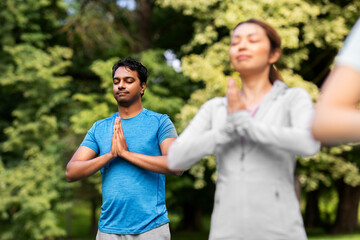 fitness, sport and healthy lifestyle concept - group of happy people doing yoga at summer park