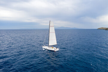 Naklejka premium Sailing boat with white sails, cloudy sky and rippled sea background