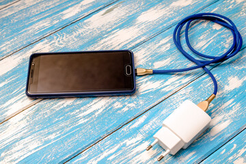 Mobile phone and charger on blue wooden background
