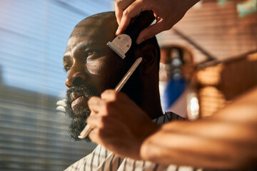 Professional barber trimming client beard in barbershop